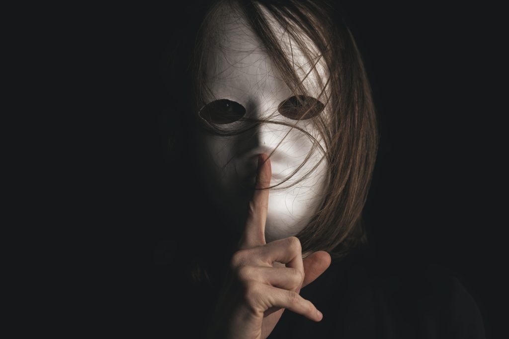 Person in white mask making shushing gesture