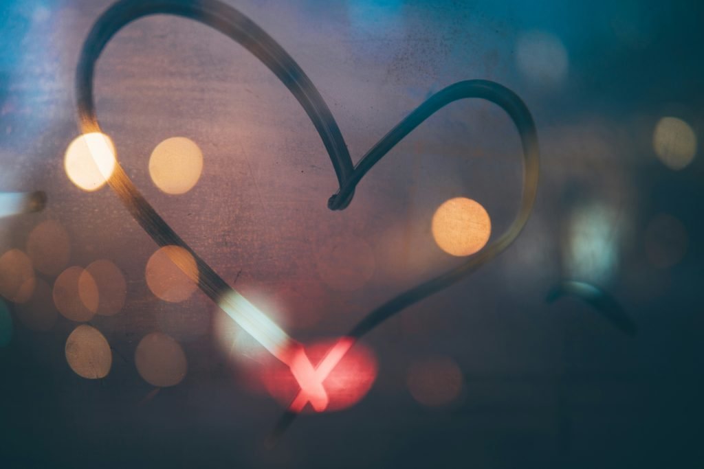 Heart drawn on foggy window with bokeh lights